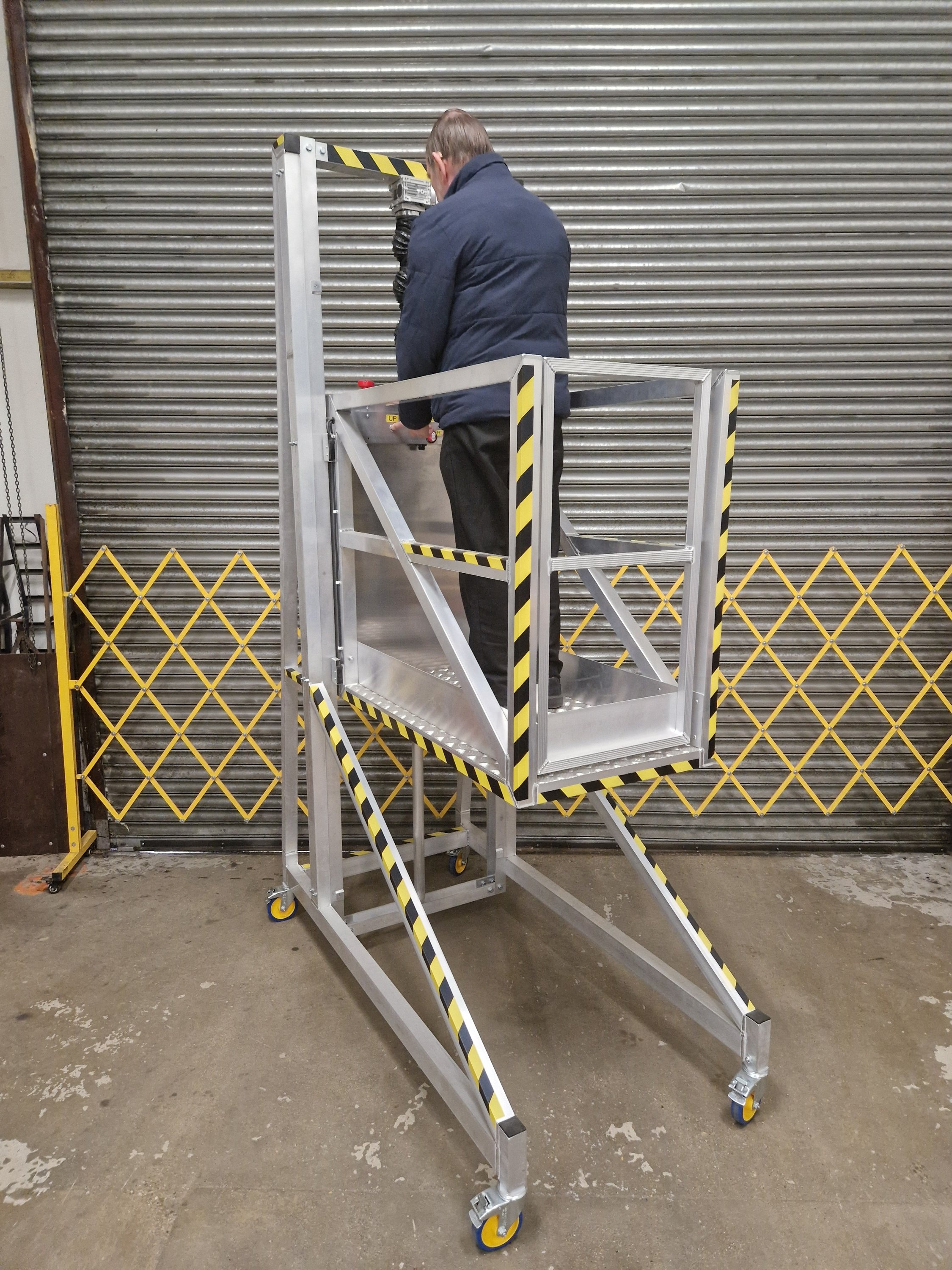 Worker standing on mobile access platform performing working at height task safely at approximately 1.5m platform height in industrial warehouse.