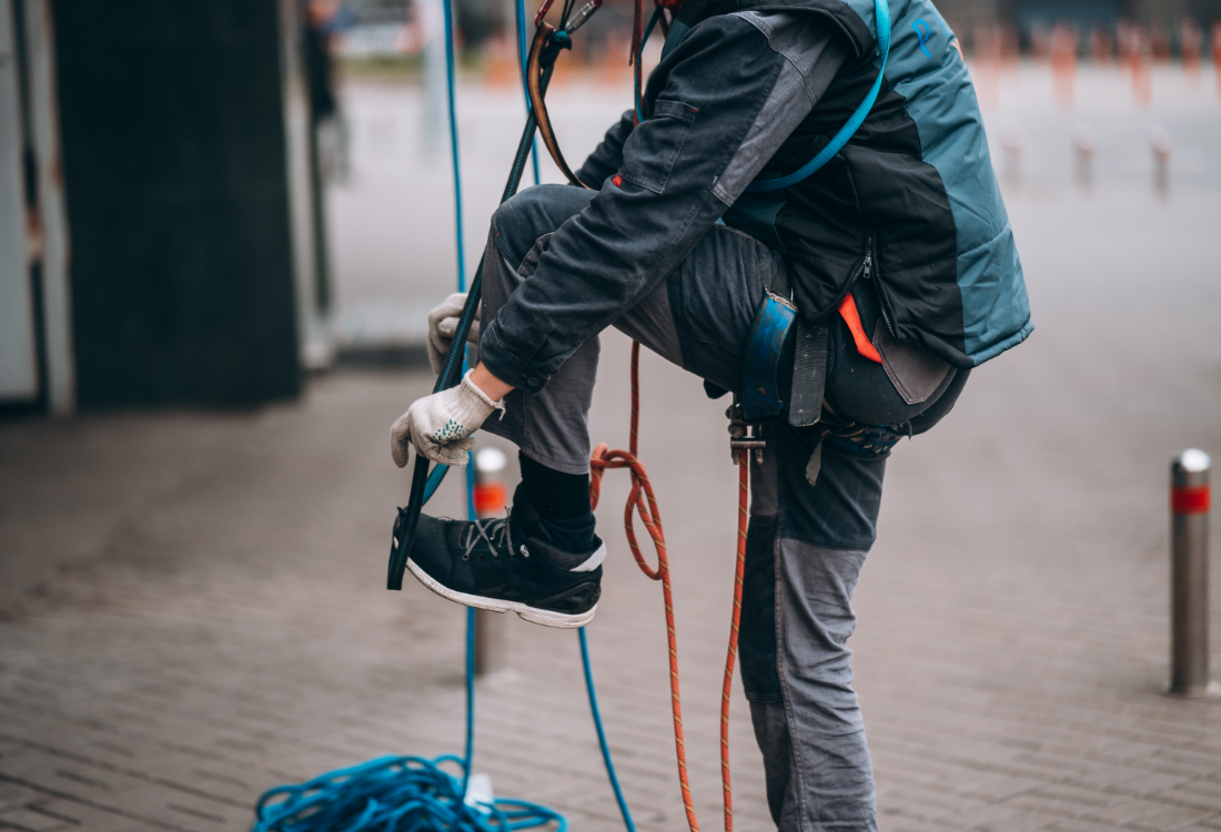 Worker wearing a safety harness and ropes while working at height outdoors.