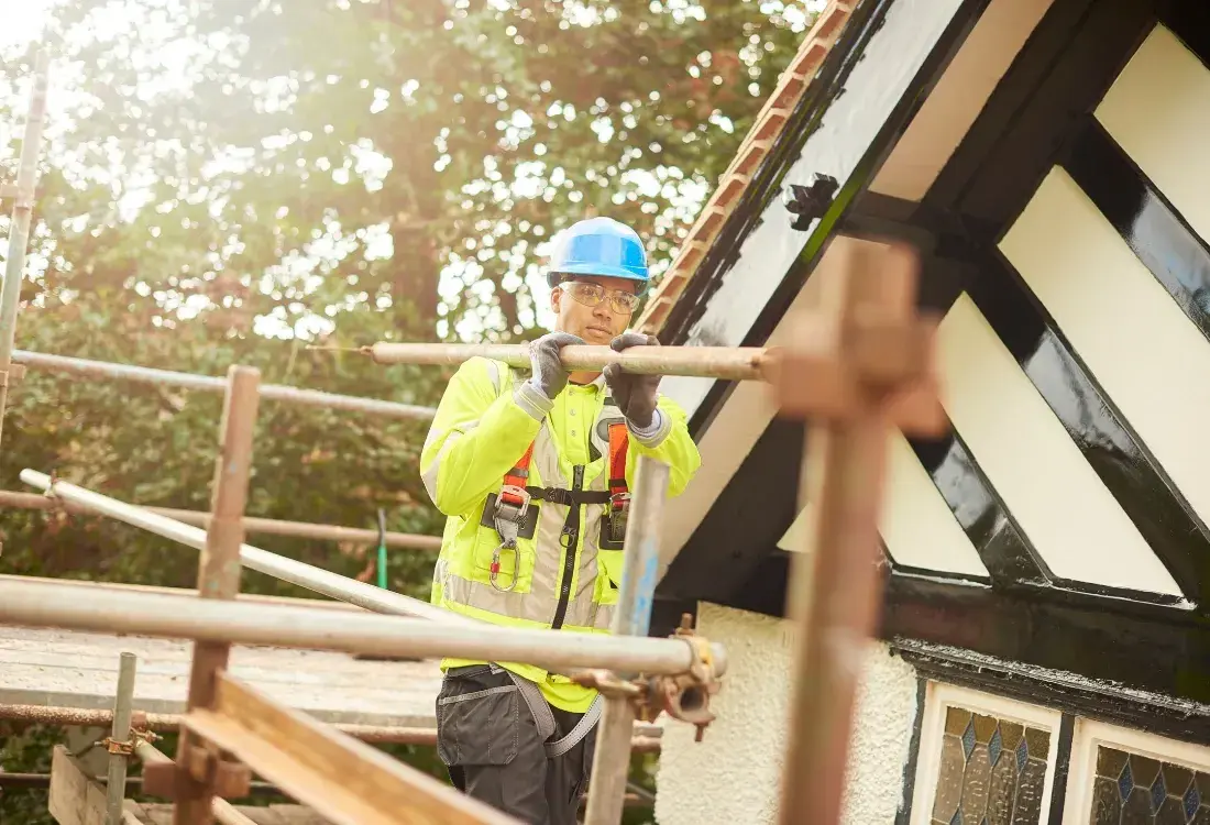 Construction worker carrying an aluminium scaffolding tube on his way to build a portable scaffolding tower.