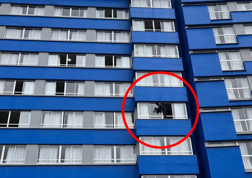 A man hanging out his window to wash it, working from height in a dangerous way