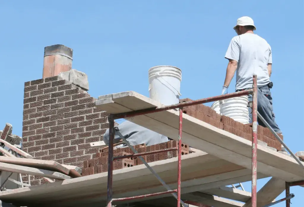 Two men working on rebuilding a chimney standing on scaffolding.