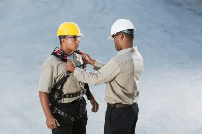 A manager training the construction worker on fall arrest and safety harness systems when working at height.