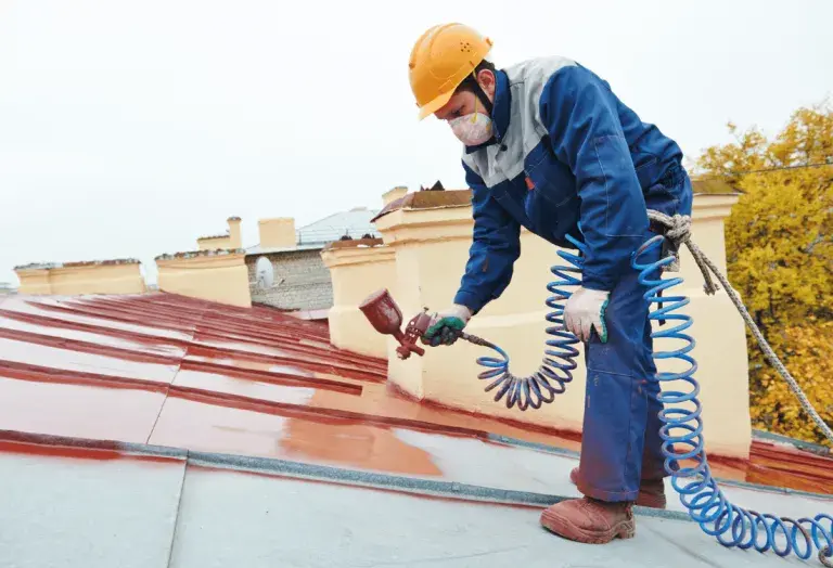 A man painting a roof after receiving roof safety training to help him stay safe.