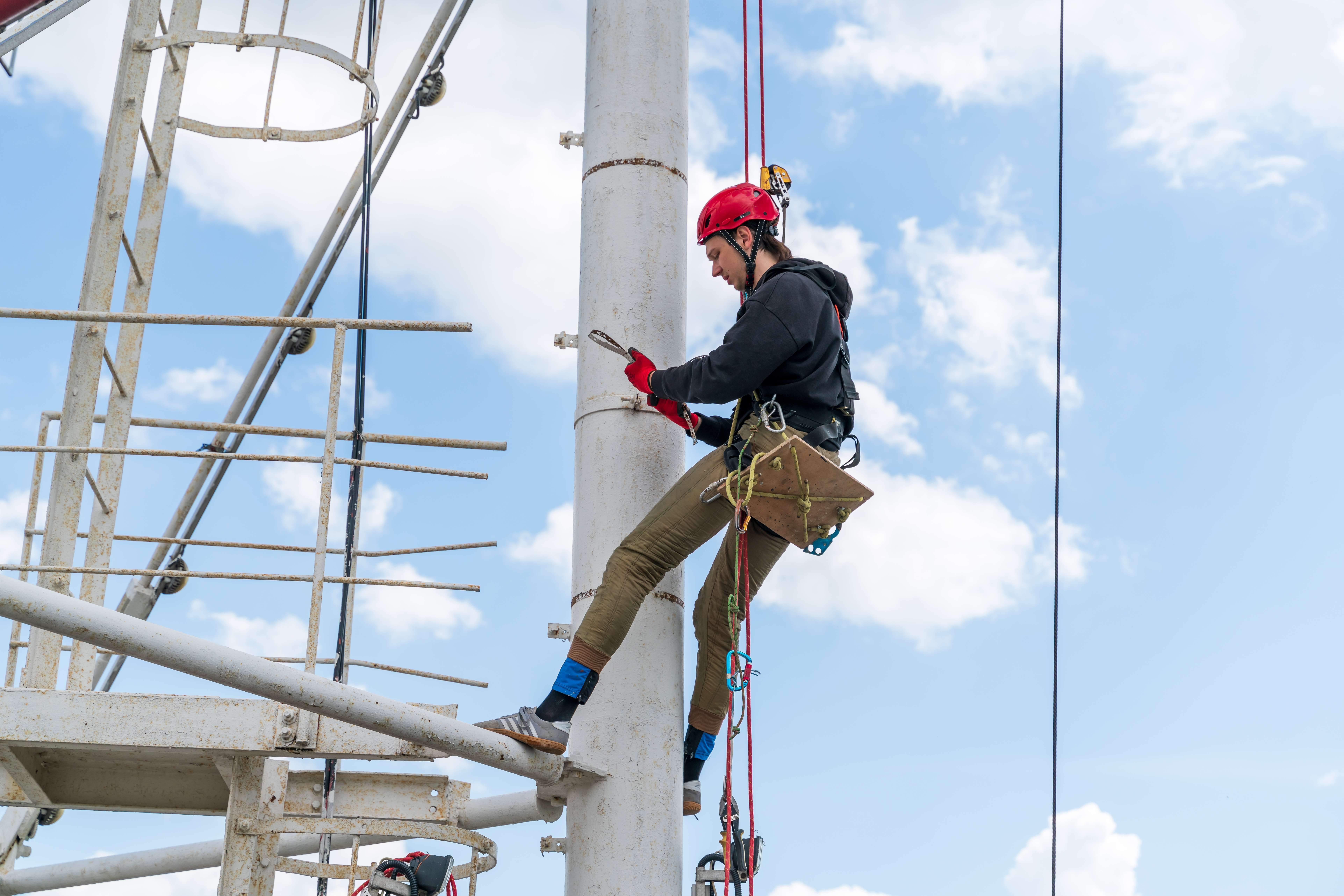 A worker inspecting work at height safety equipment including harness and lanyard on construction site.