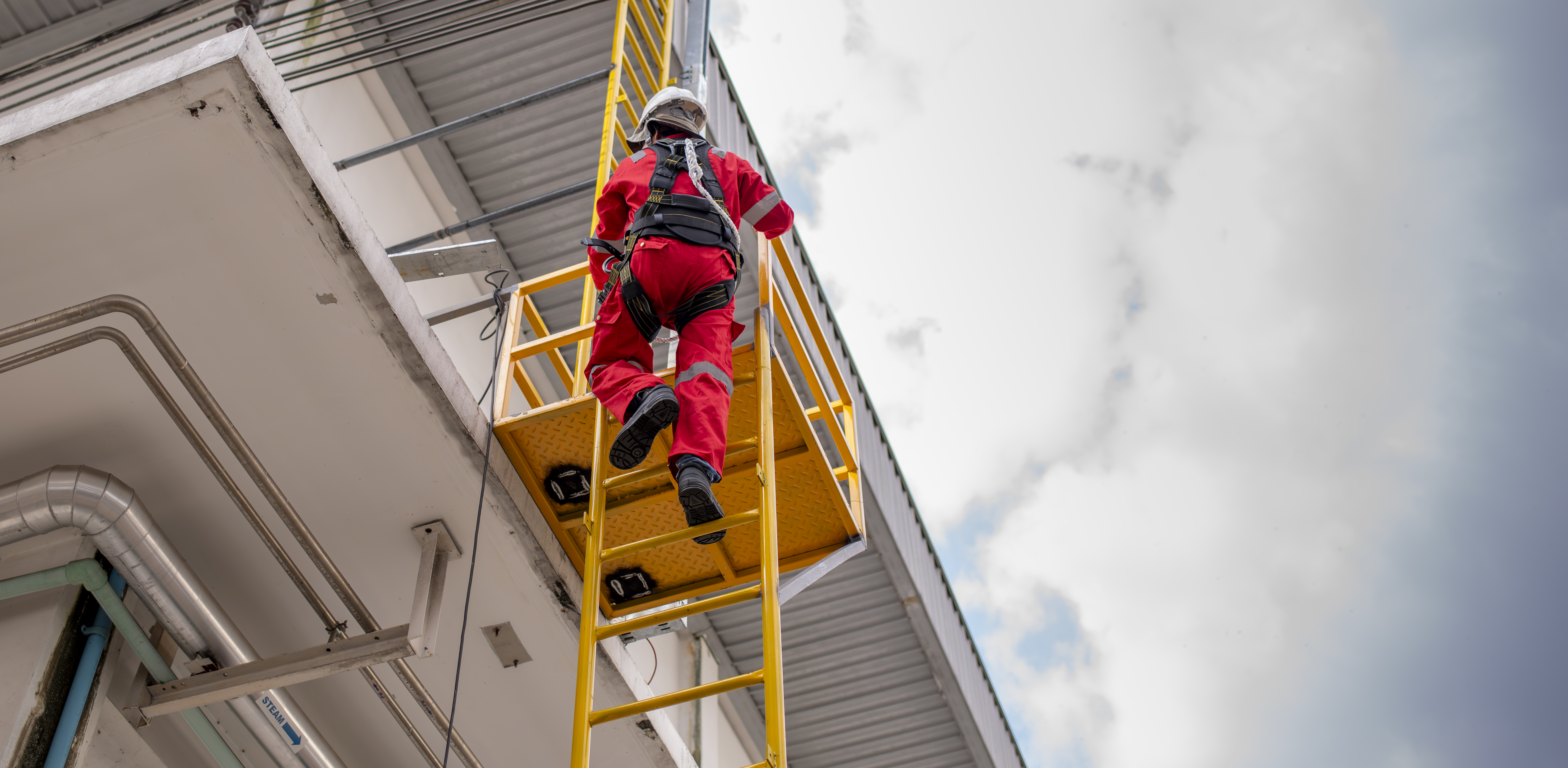 A worker using desksurfer platform outdoors in summer conditions on building exterior surface.