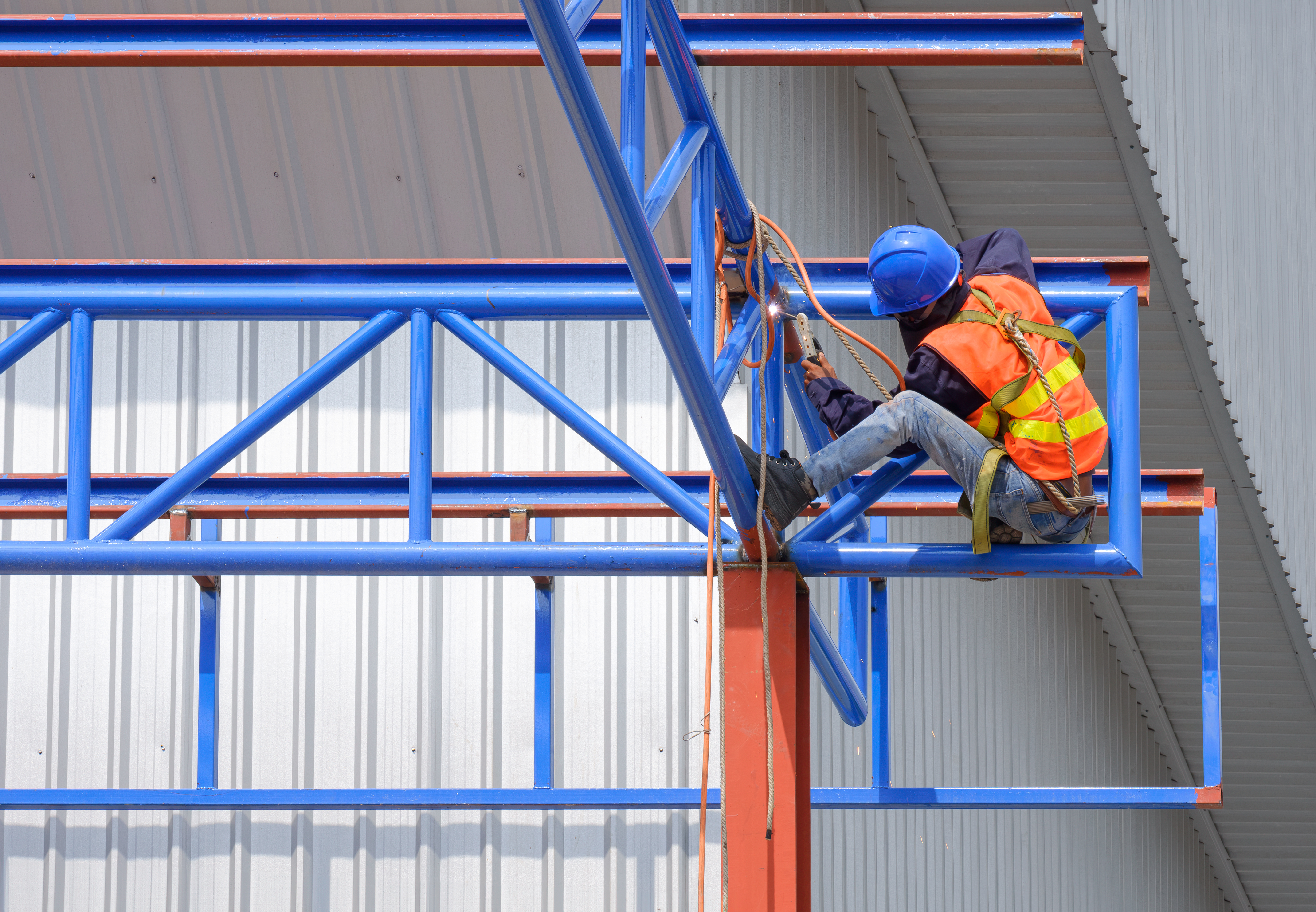 Worker using safety harness performing welding task at height on steel framework demonstrating importance of edge protection in fall prevention.